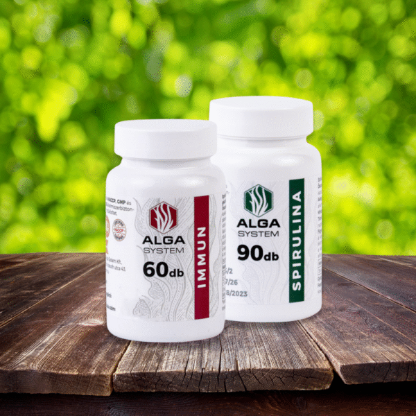 Alga System Spirulina és Immun kapszulák fehér műanyag dobozban, fa felületen, zöld lombos háttérrel.