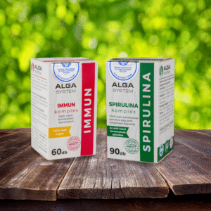 Alga System Spirulina és Immun Komplex étrendkiegészítők dobozban, fa felületen, zöld lombos háttérrel.