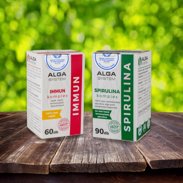 Alga System Spirulina és Immun Komplex étrendkiegészítők dobozban, fa felületen, zöld lombos háttérrel.