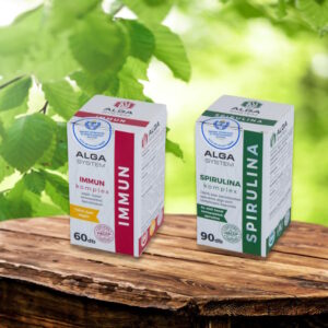 Alga System Spirulina és Immun Komplex étrendkiegészítők dobozban, fa felületen, zöld lombos háttérrel.