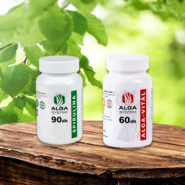 Alga System Spirulina és Alga-Vitál kapszulák fehér műanyag dobozban, fa felületen, zöld lombozattal a háttérben, természetes környezetben.