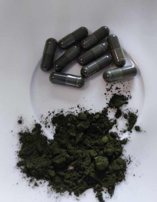 Chlorella alga por és zöld kapszulák fehér tálon.