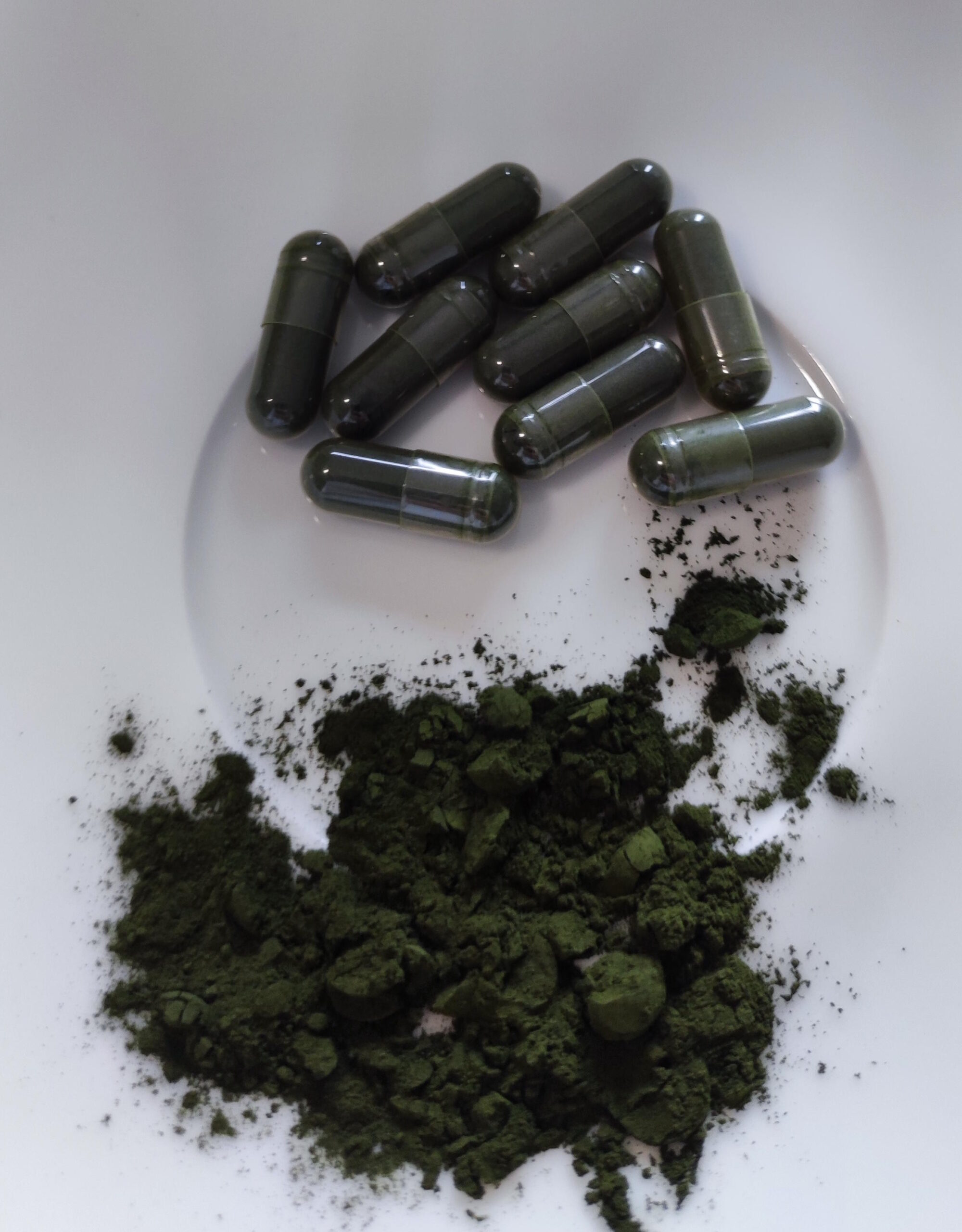 Chlorella alga por és zöld kapszulák fehér tálon.